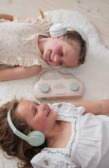 deux soeurs souriantes, étendues sur un tapis conforable, qui écoutent avec leurs écouteurs, les histoires diffusées par leur boîte à rêves de cloudb